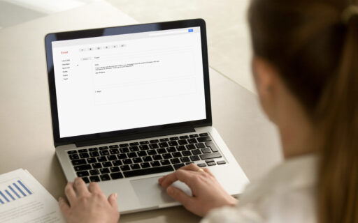 Image of Businesswoman typing e-mail on laptop at office desk, composing professional email letter using business etiquette, writing e message to corporate client online, focus on screen, close up rear view