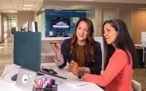 two women collaborating in front of a computer in the workplace