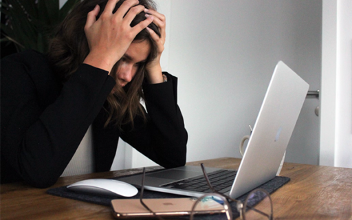 Woman with brown hair resting hand on her head in frustration while looking at a laptop screen.