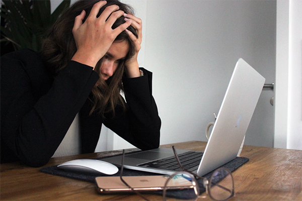 Woman with brown hair resting hand on her head in frustration while looking at a laptop screen.